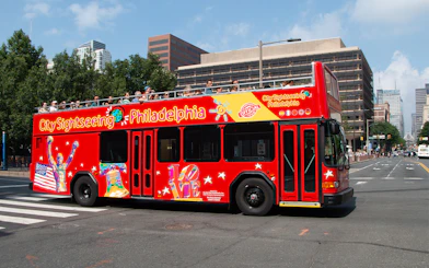 Red double-decker bus on Philadelphia Hop-On-Hop-Off Tour with city buildings in background.