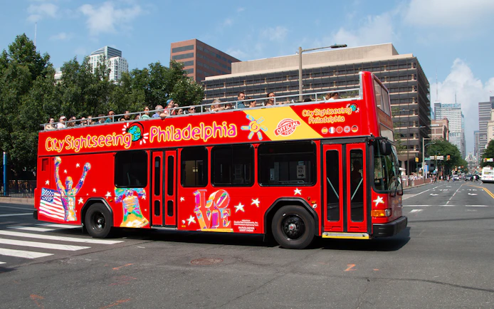 Red double-decker bus on Philadelphia Hop-On-Hop-Off Tour with city buildings in background.