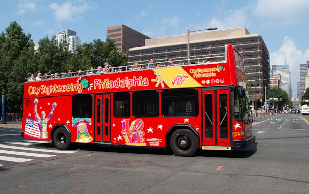 Red double-decker bus on Philadelphia Hop-On-Hop-Off Tour with city buildings in background.