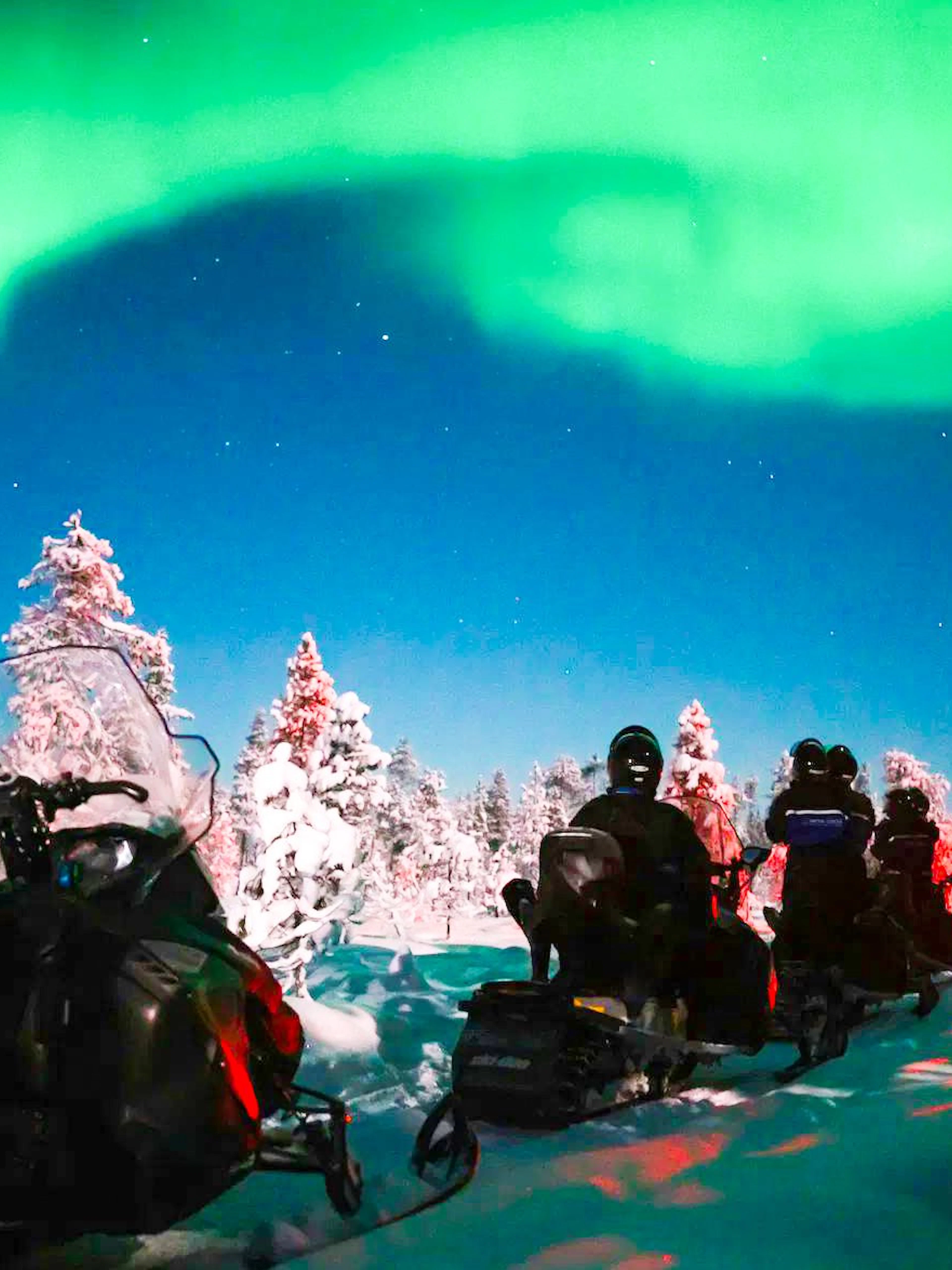 Snowmobile ride under Northern Lights in snowy forest, Levi, Finland.