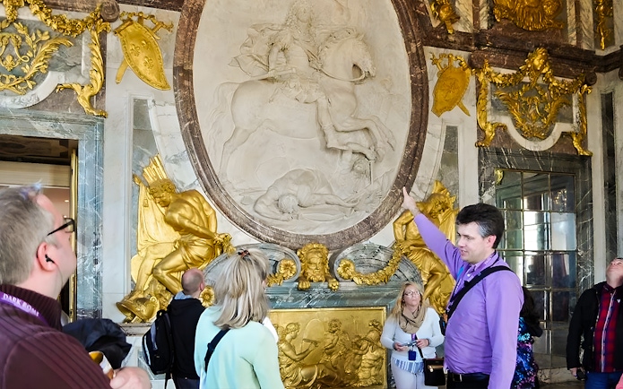 Tour guide explaining artwork inside Versailles Palace to visitors.