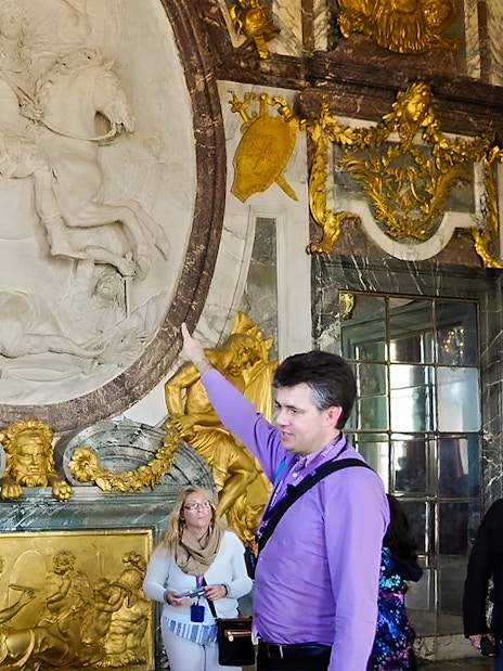 Tour guide explaining artwork inside Versailles Palace to visitors.
