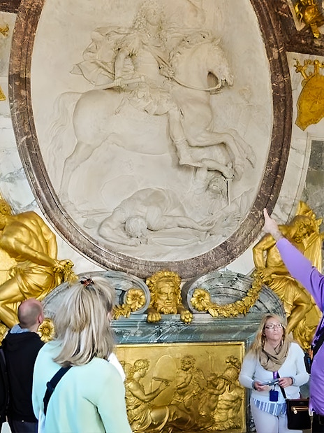 Tour guide explaining artwork inside Versailles Palace to visitors.