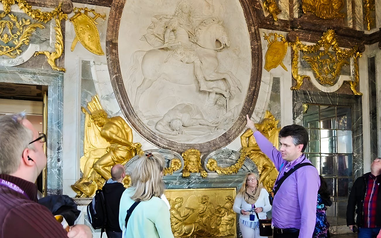 Tour guide explaining artwork inside Versailles Palace to visitors.