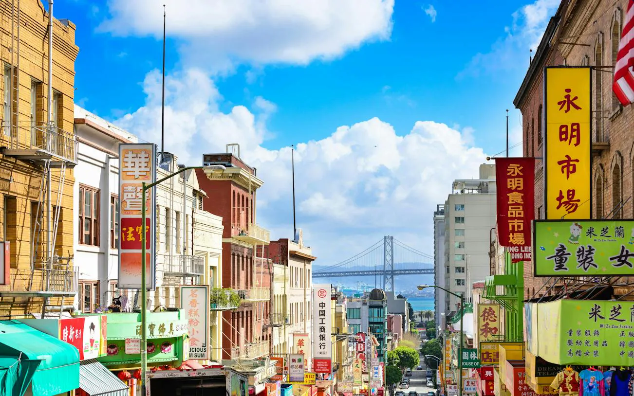 San Francisco Chinatown street view with colorful signs and Bay Bridge in the background.