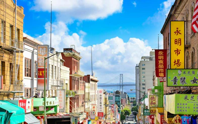 San Francisco Chinatown street view with colorful signs and Bay Bridge in the background.