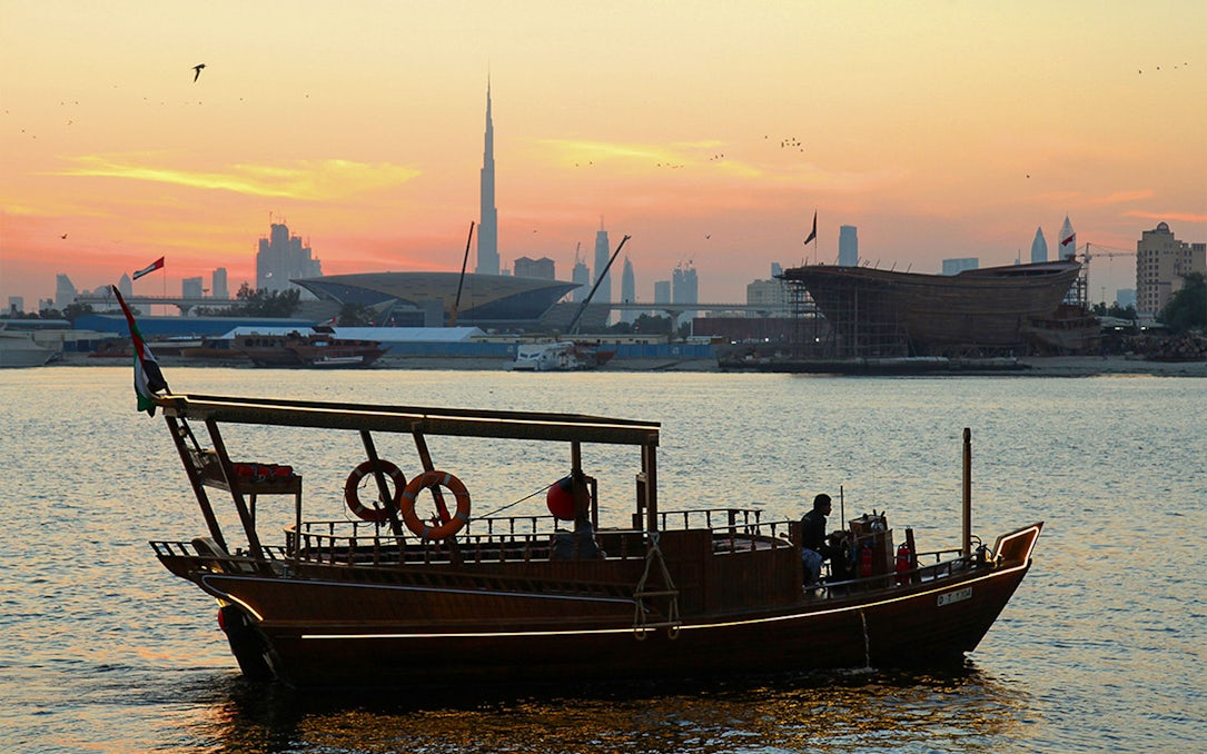 Abra boat on Dubai Creek at sunset with Burj Khalifa in the background.