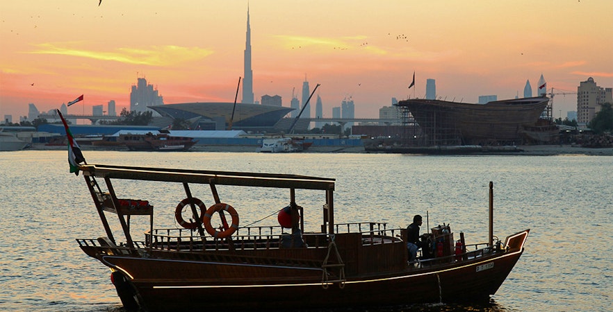 Abra boat on Dubai Creek at sunset with Burj Khalifa in the background.