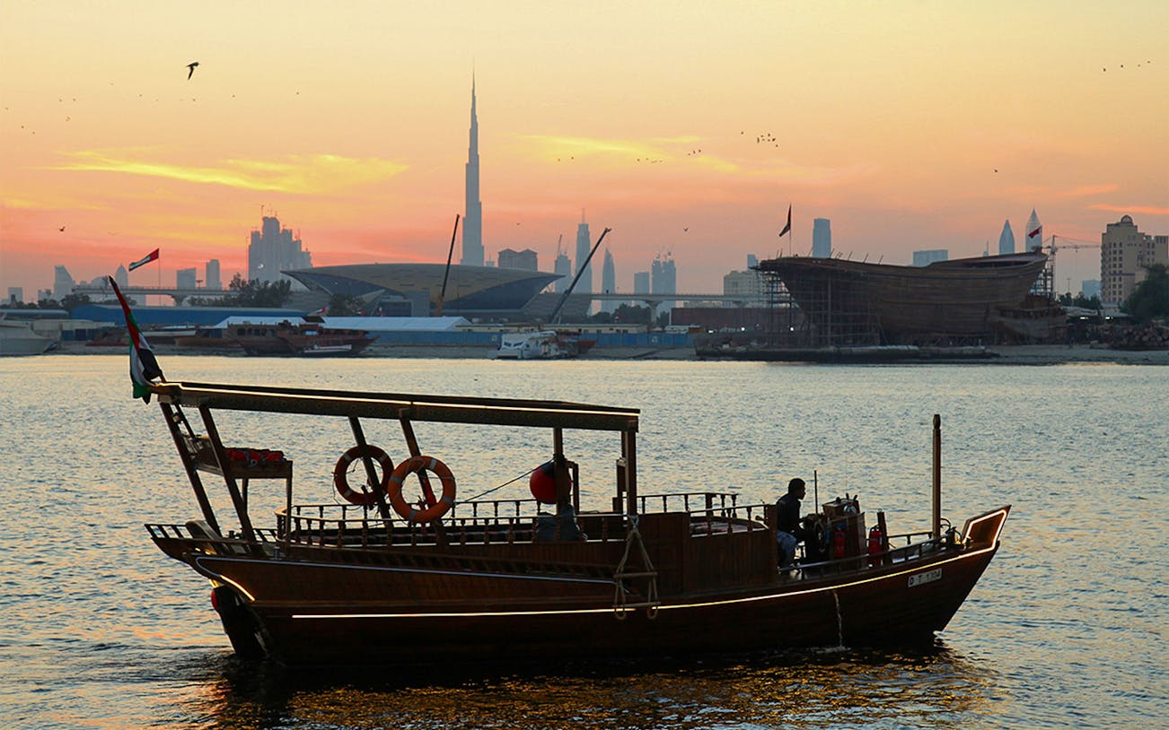 Abra boat on Dubai Creek at sunset with Burj Khalifa in the background.