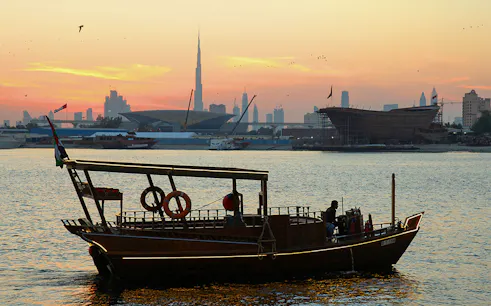 Abra boat on Dubai Creek at sunset with Burj Khalifa in the background.