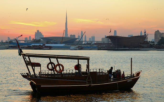 Abra boat on Dubai Creek at sunset with Burj Khalifa in the background.
