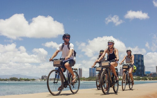 Cyclists enjoying a scenic ride along the waterfront in Oahu with city skyline views.