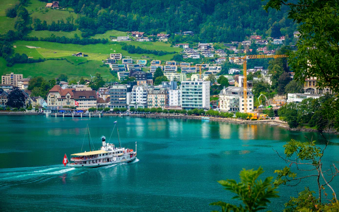 Paddle steamer on Lake Lucerne with Brunnen town, Swiss flag, and Alpine hills in Central Switzerland.