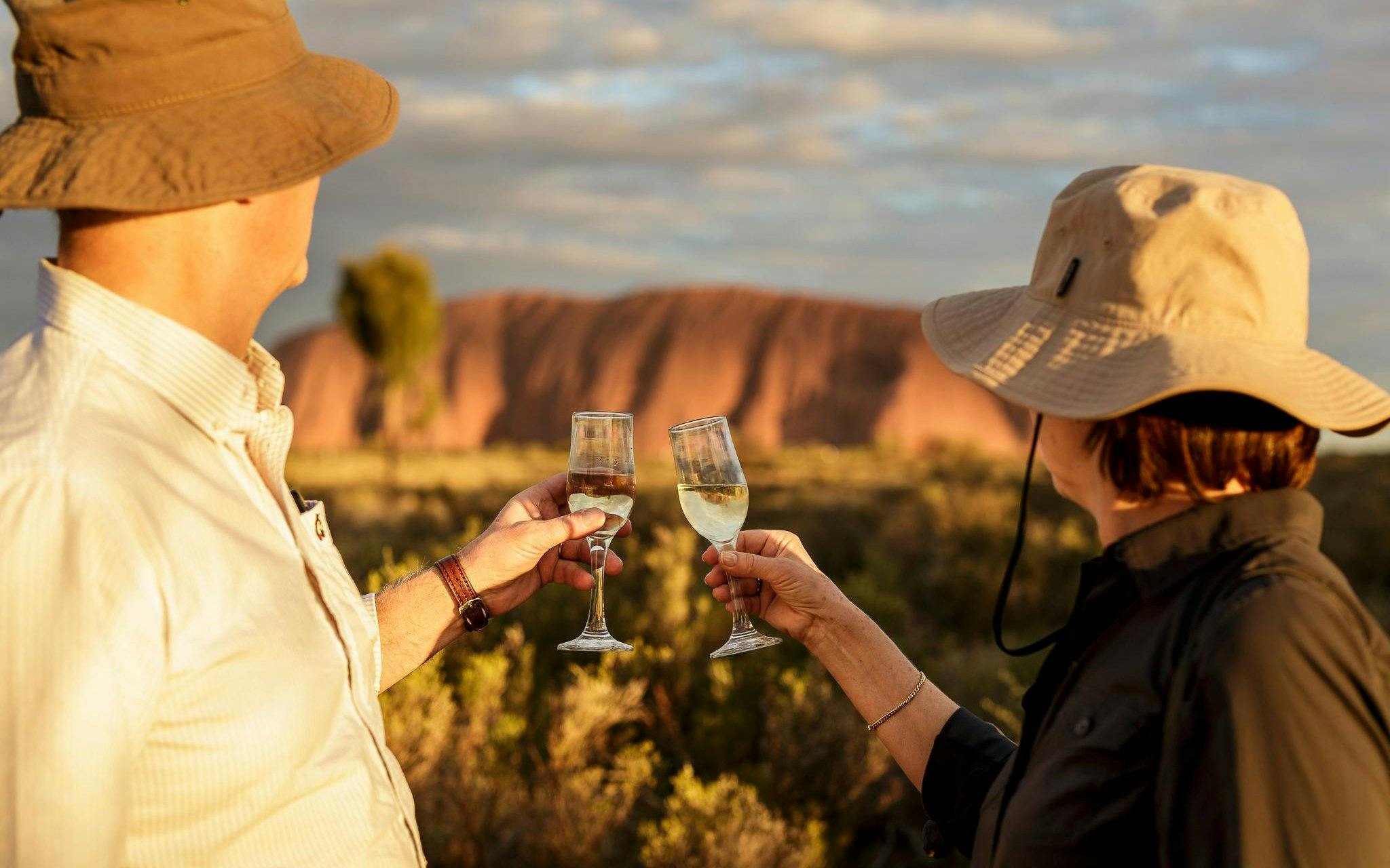 Tourists toasting with wine glasses at sunset in front of Uluru, Australia.