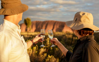 Tourists toasting with wine glasses at sunset in front of Uluru, Australia.