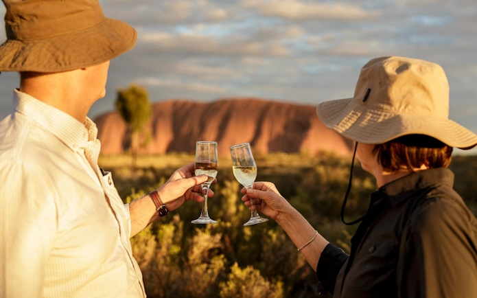 Tourists toasting with wine glasses at sunset in front of Uluru, Australia.