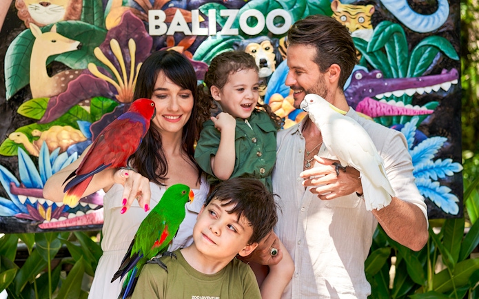 Family enjoying colorful parrots at Bali Zoo entrance.