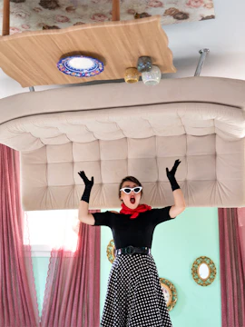 Person in vintage attire inside Upside Down House Melaka with furniture on ceiling.