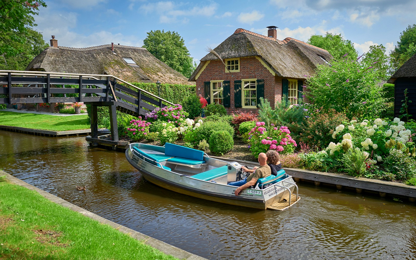 Giethoorn canal boat ride with tourists, traditional Dutch village houses, Netherlands.