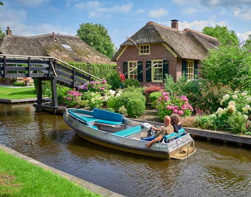 Boat ride on Giethoorn canal passing traditional Dutch house and garden, Netherlands.