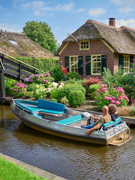 Boat ride on Giethoorn canal passing traditional Dutch house and garden, Netherlands.