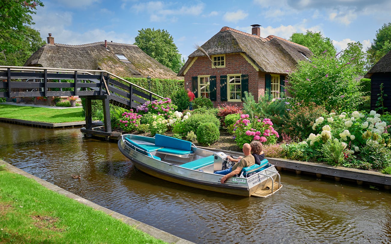 Boat ride on Giethoorn canal passing traditional Dutch house and garden, Netherlands.