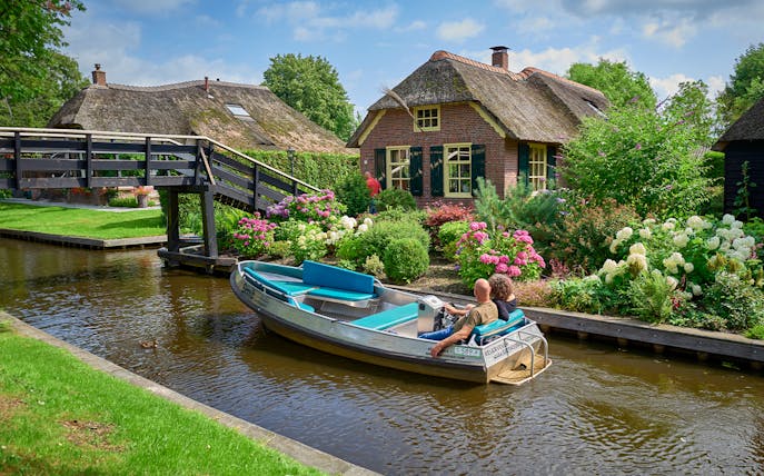 Boat ride on Giethoorn canal passing traditional Dutch house and garden, Netherlands.