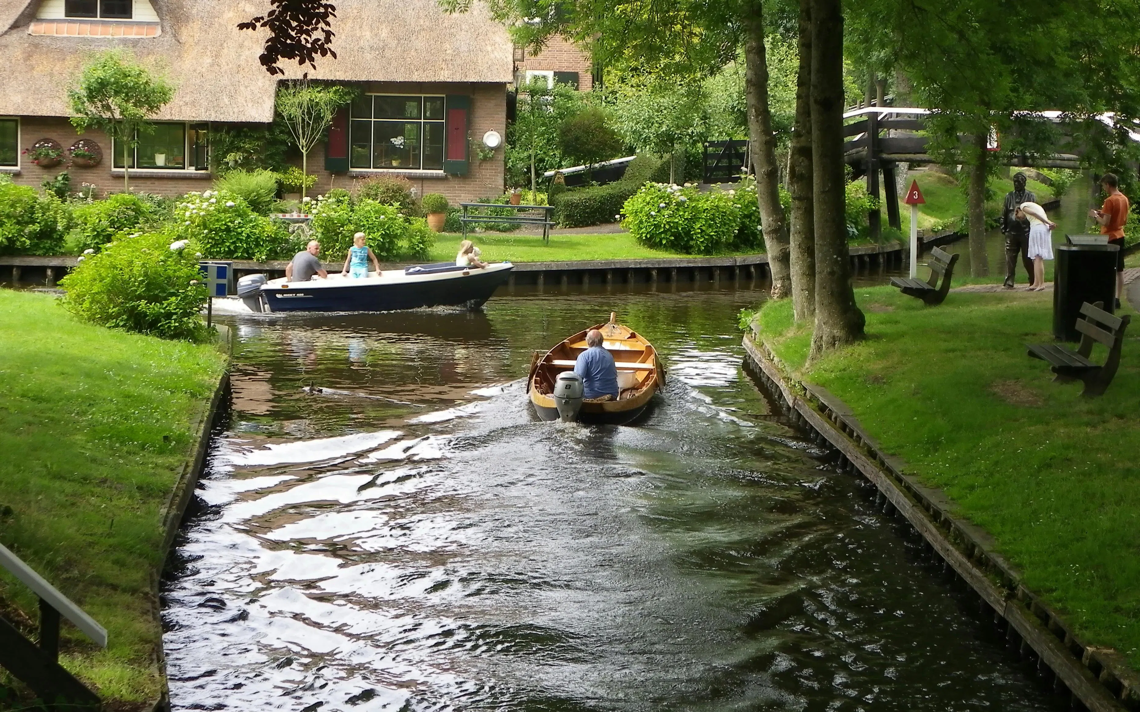 Boats navigating a canal in Giethoorn, Netherlands, with lush greenery and traditional houses.