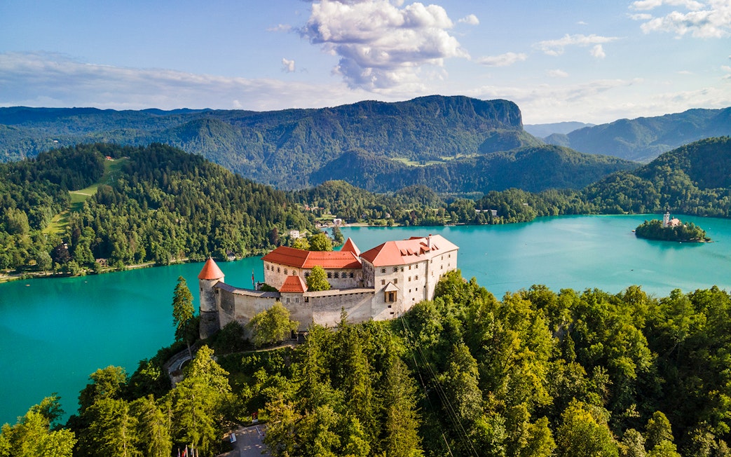 Bled Castle overlooking Lake Bled with surrounding forest and mountains in Slovenia.