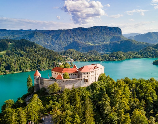 Bled Castle overlooking Lake Bled with surrounding forest and mountains in Slovenia.
