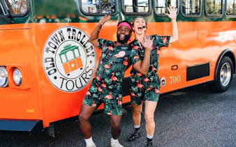 People in matching outfits posing excitedly in front of a Savannah trolley.