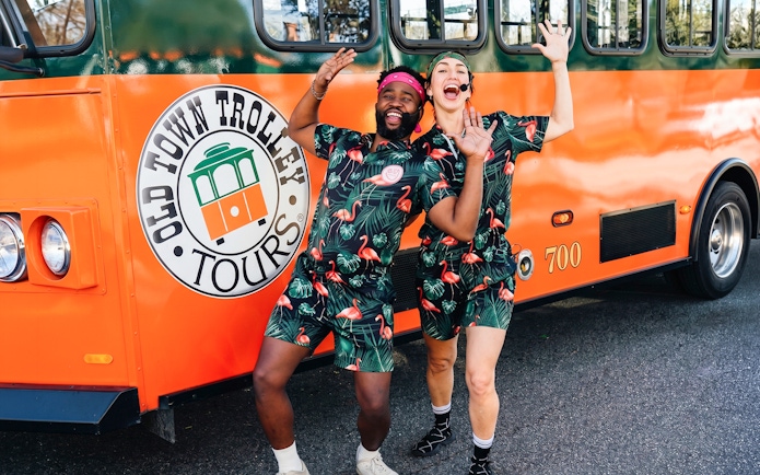 People in matching outfits posing excitedly in front of a Savannah trolley.