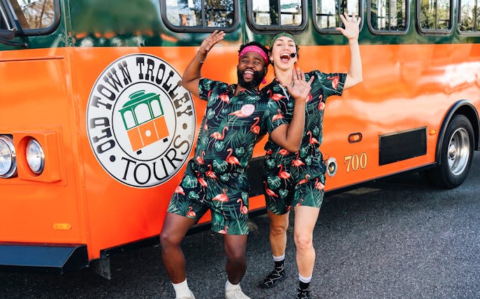People in matching outfits posing excitedly in front of a Savannah trolley.