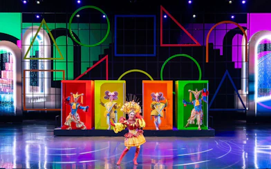 Performers in colorful costumes on stage at a vibrant Colosseum show.
