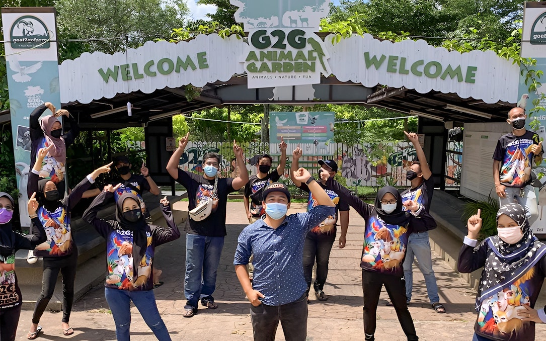 Visitors at G2G Animal Garden entrance, wearing themed shirts and masks, posing cheerfully.