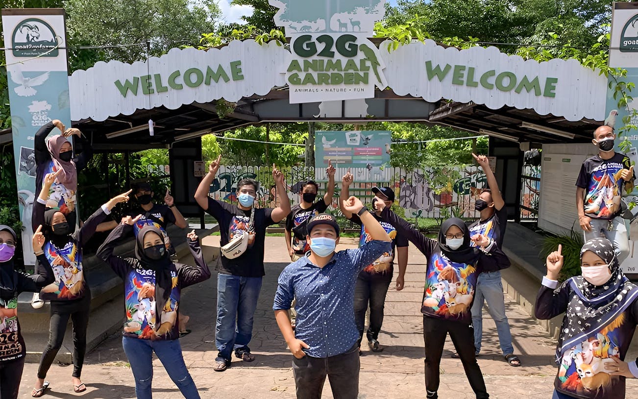 Visitors at G2G Animal Garden entrance, wearing themed shirts and masks, posing cheerfully.