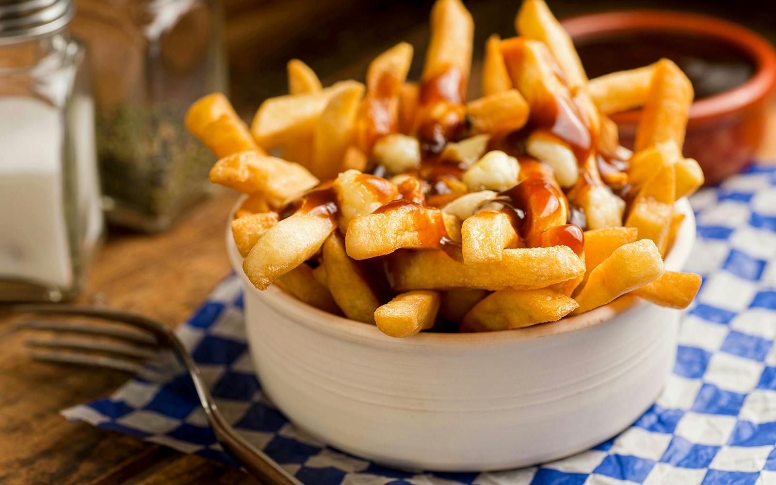 Poutine with fries, cheese curds, and gravy in a bowl on a checkered napkin.