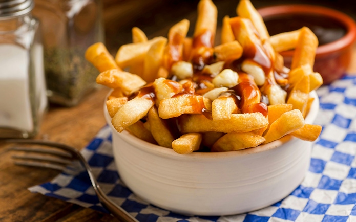 Poutine with fries, cheese curds, and gravy in a bowl on a checkered napkin.