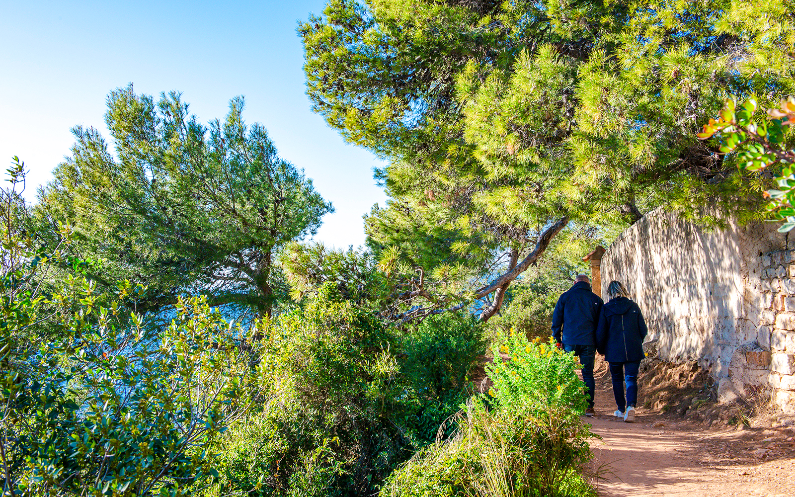 Couple walking on Sentier du Littoral trail in winter, surrounded by lush greenery.