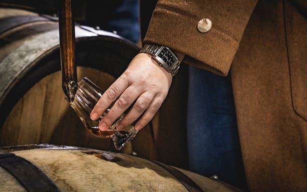 Hand pouring whiskey from barrel during Tasmania distillery tour, Hobart.