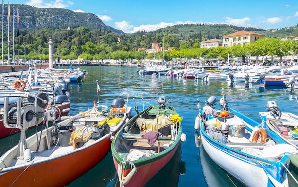 Boats docked at Lake Garda with scenic hills and buildings in the background.
