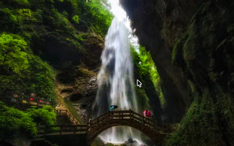 Waterfall cascading in Wulong Three Natural Bridges, Chongqing, with tourists on a wooden bridge.