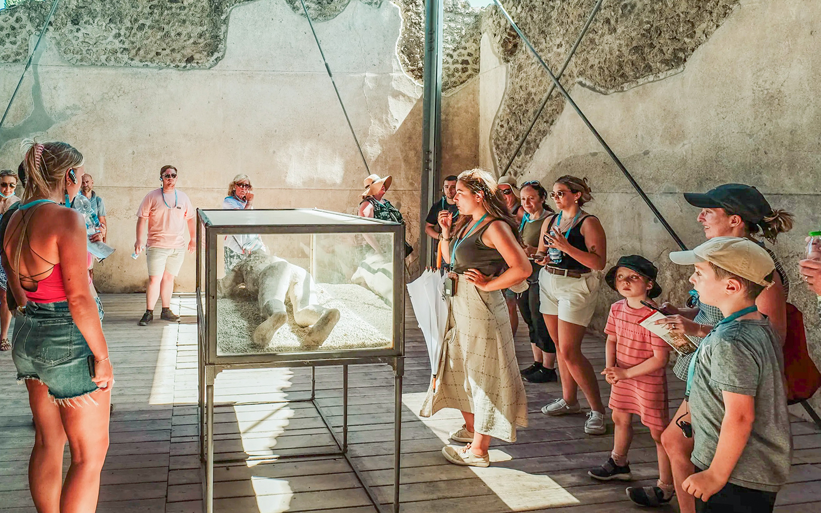 Tour group observing a plaster cast of a victim at Pompeii with a guide explaining.
