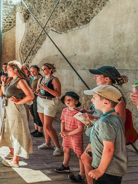 Tour group observing a plaster cast of a victim at Pompeii with a guide explaining.