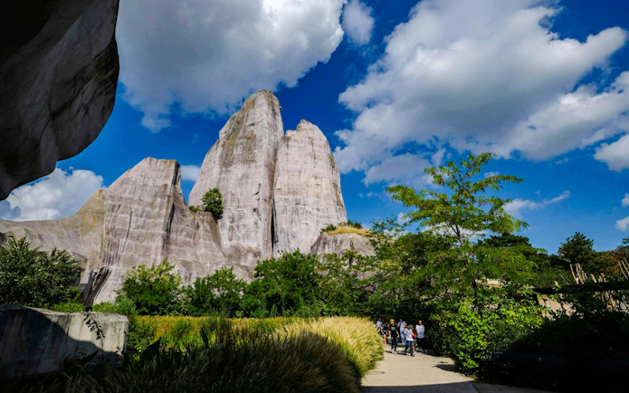 Pathway through lush greenery at Vincennes Zoo with rock formations in the background.