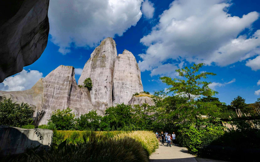 Pathway through lush greenery at Vincennes Zoo with rock formations in the background.