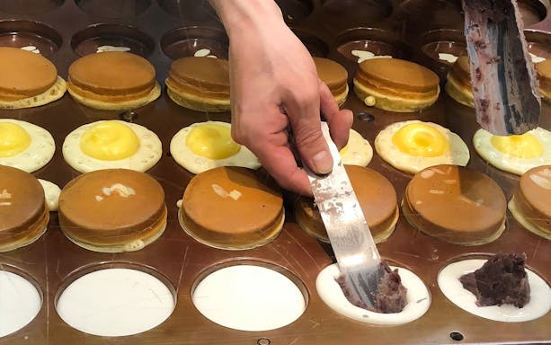 Hand preparing Japanese pancakes with sweet filling on Shibuya food tour.