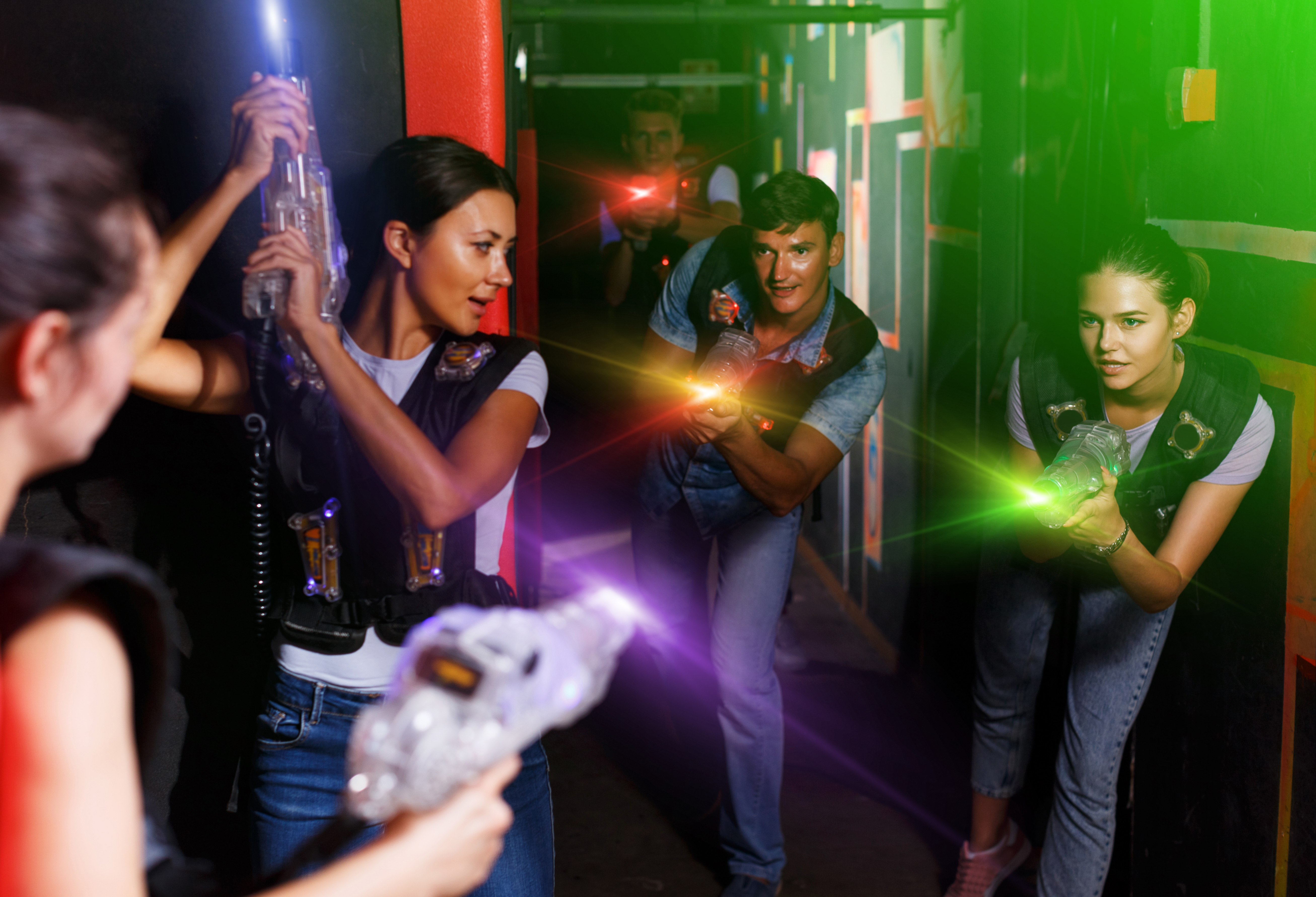 Participants playing in a laser tag arena with colorful laser beams.