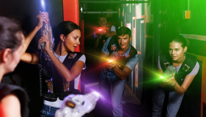 Participants playing in a laser tag arena with colorful laser beams.