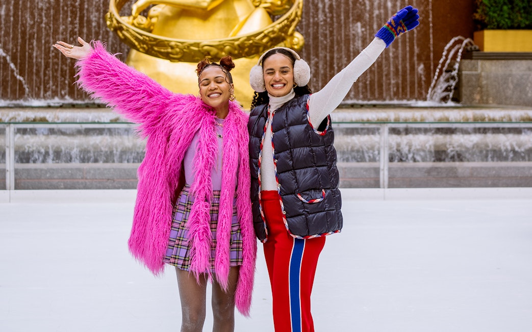 Two people ice skating at Rockefeller Center with Prometheus statue in the background.